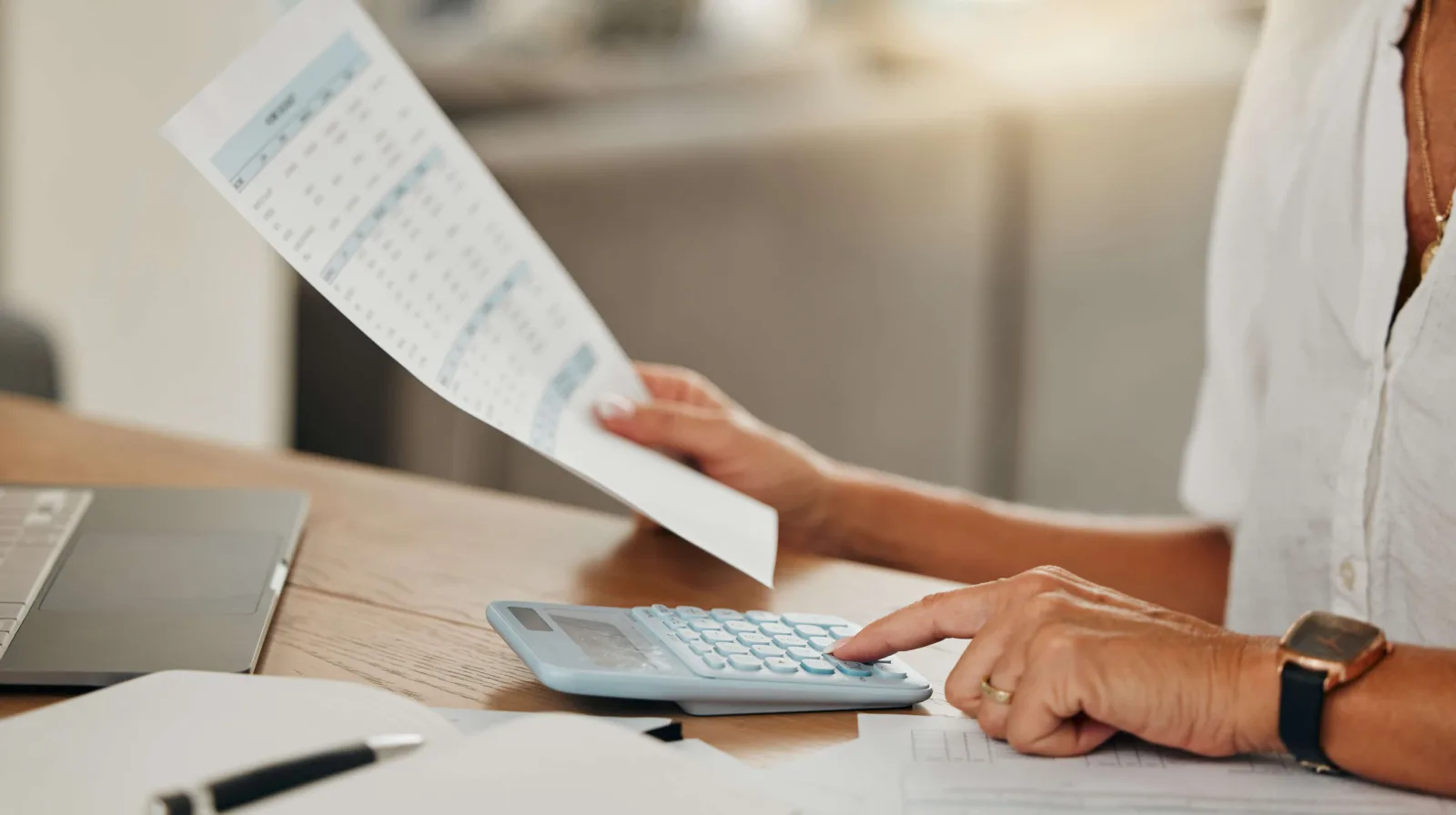 A person at a desk holding a printed calendar page beside a calculator and a notebook