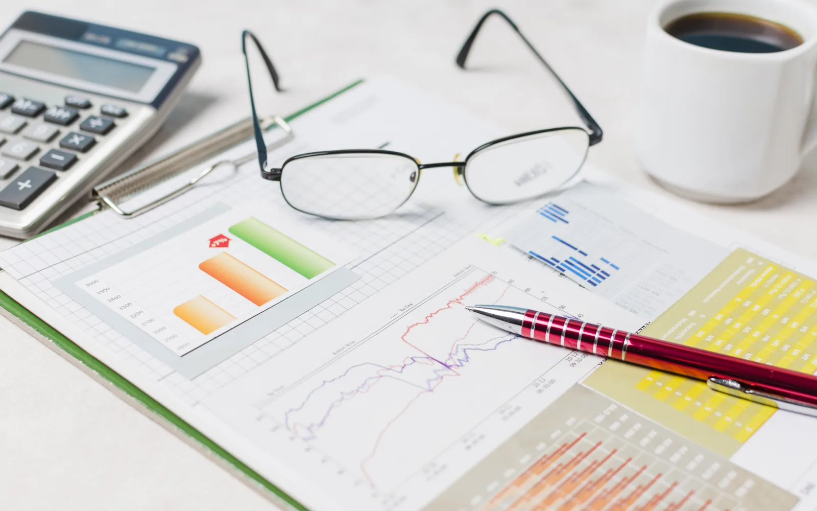 Printed financial reports and charts with a calculator, pen and reading glasses