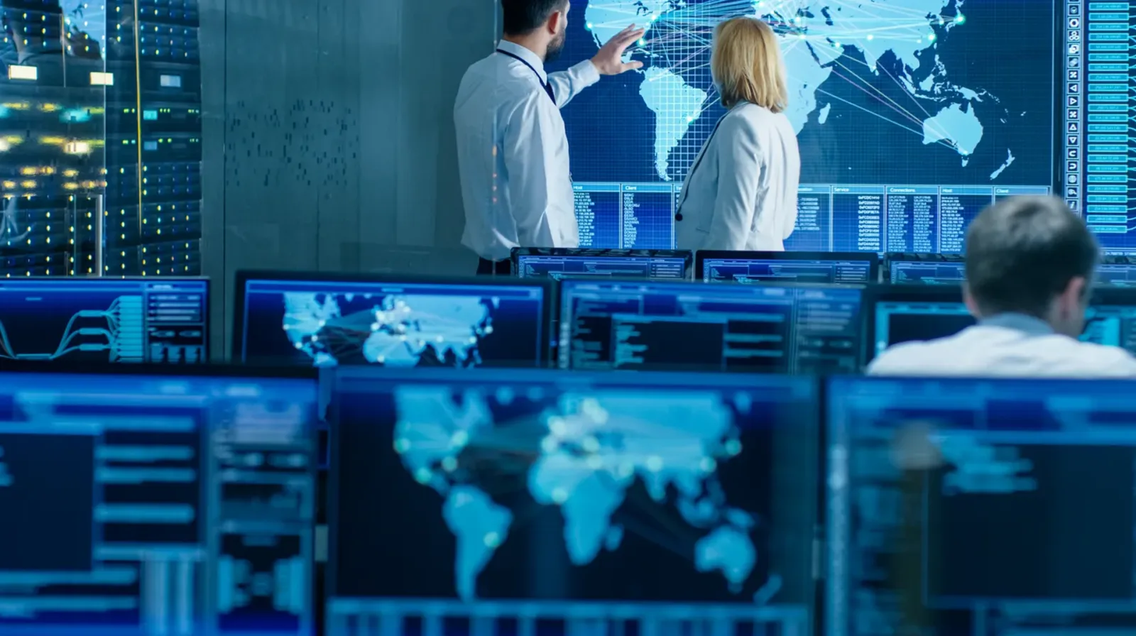Three people in a monitoring room in front of screens showing world maps