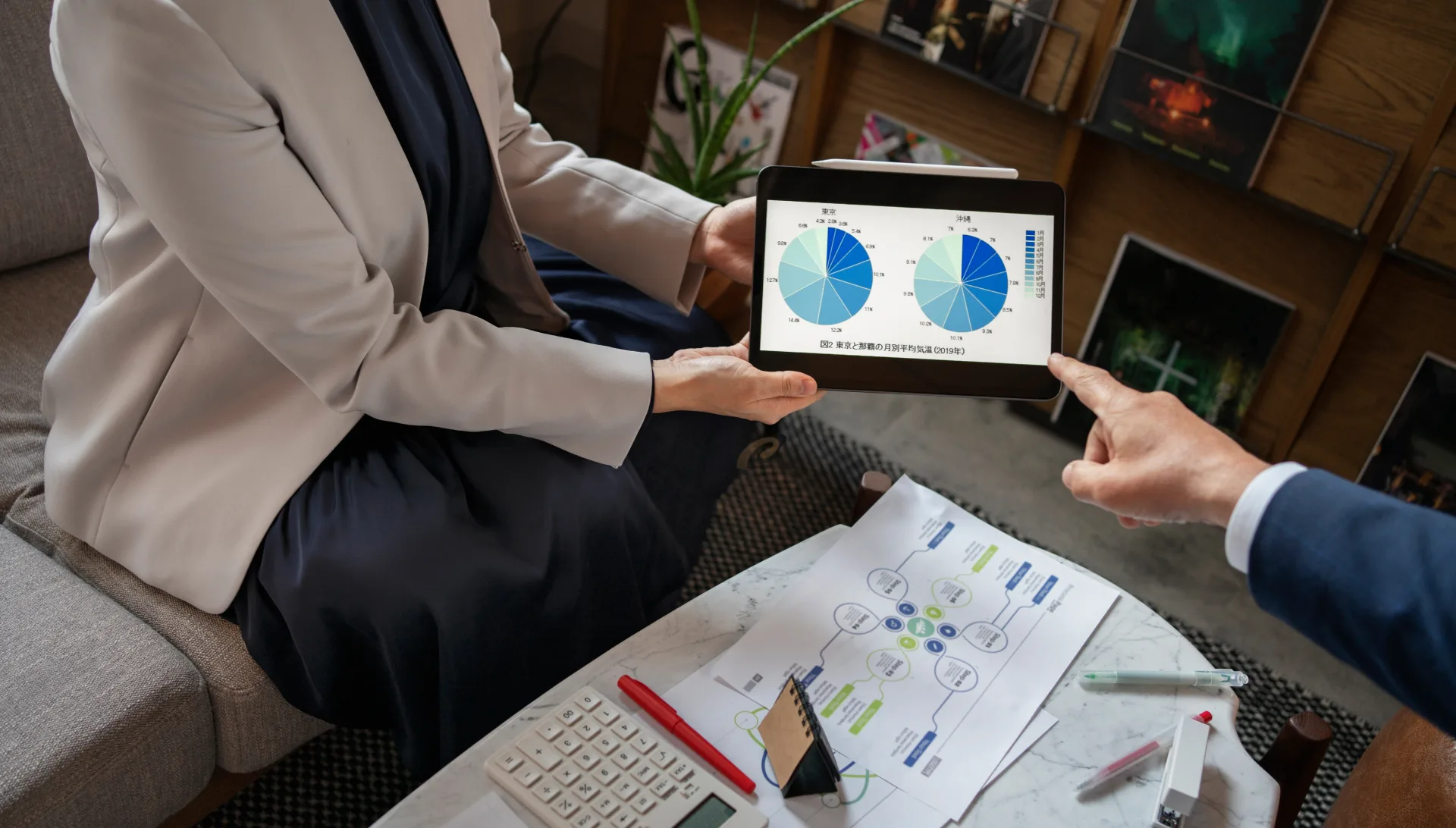 Two people reviewing charts on a tablet over printed documents and a calculator