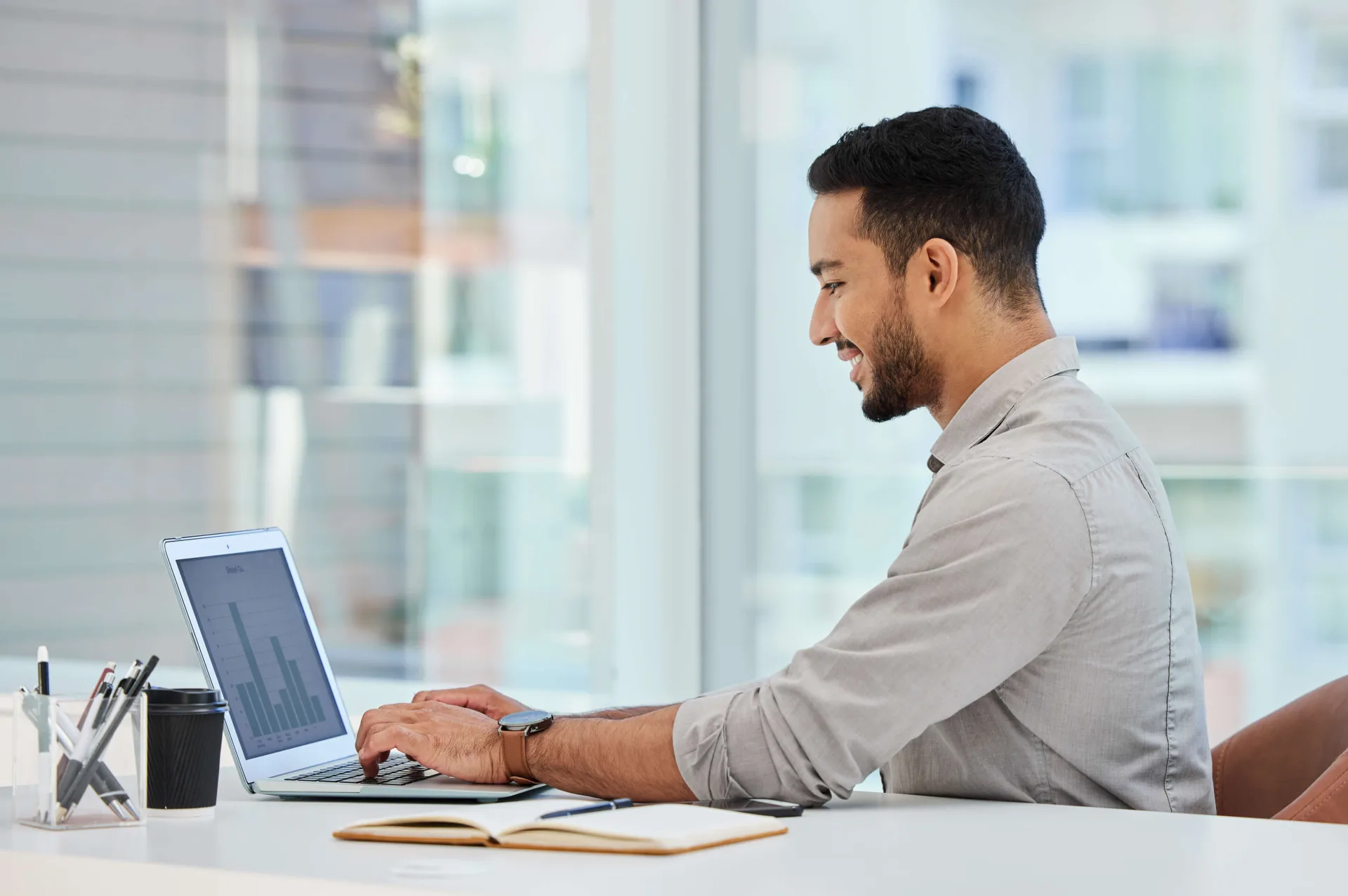 A man working at a laptop at a bright desk by a window