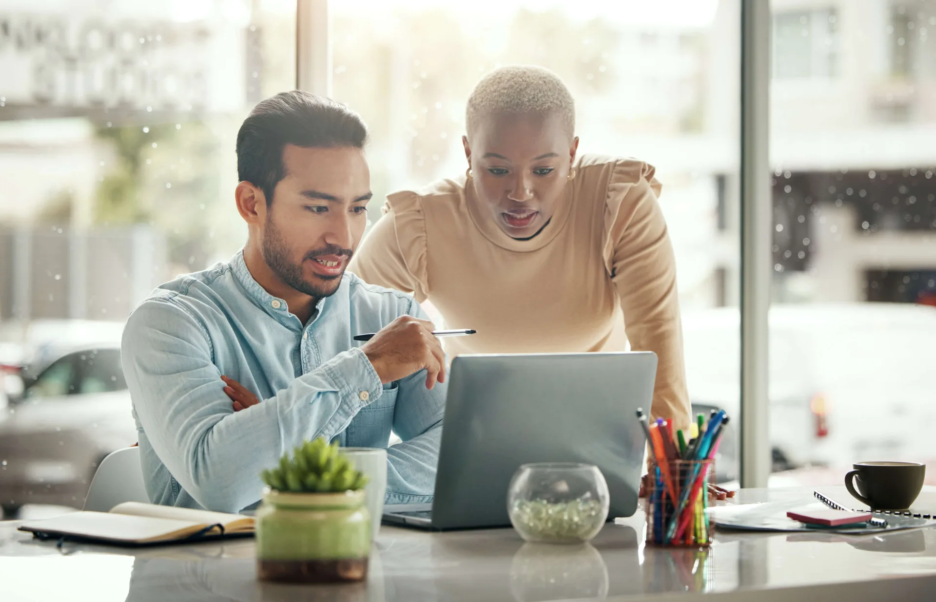 Two colleagues reviewing work on a laptop at a bright desk