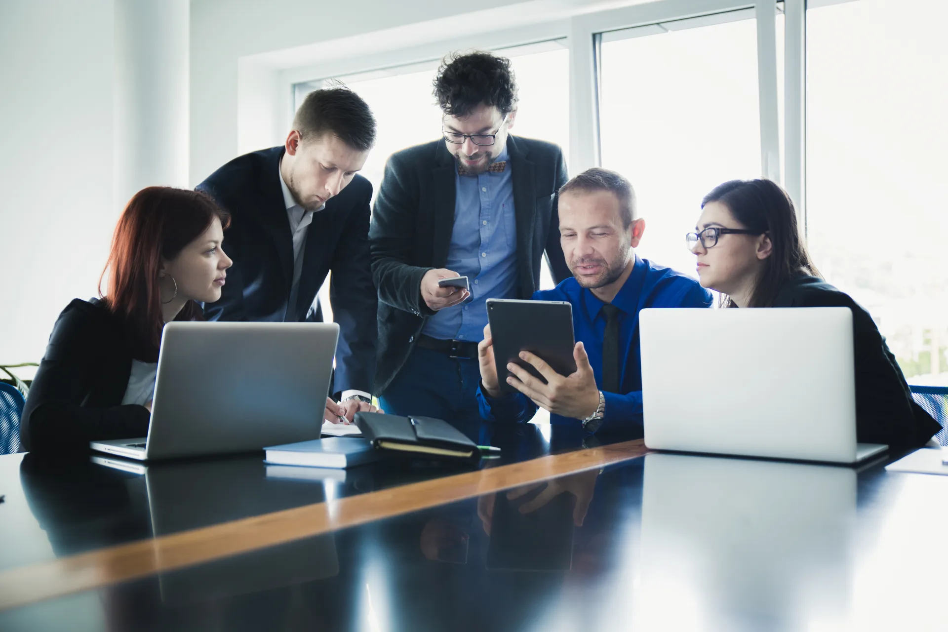 A project team gathered around laptops and a tablet at a table in a bright office